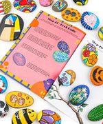Unplug And Go Outside 30-day Workbook open amid colorful hand-painted stones with positive messages and designs