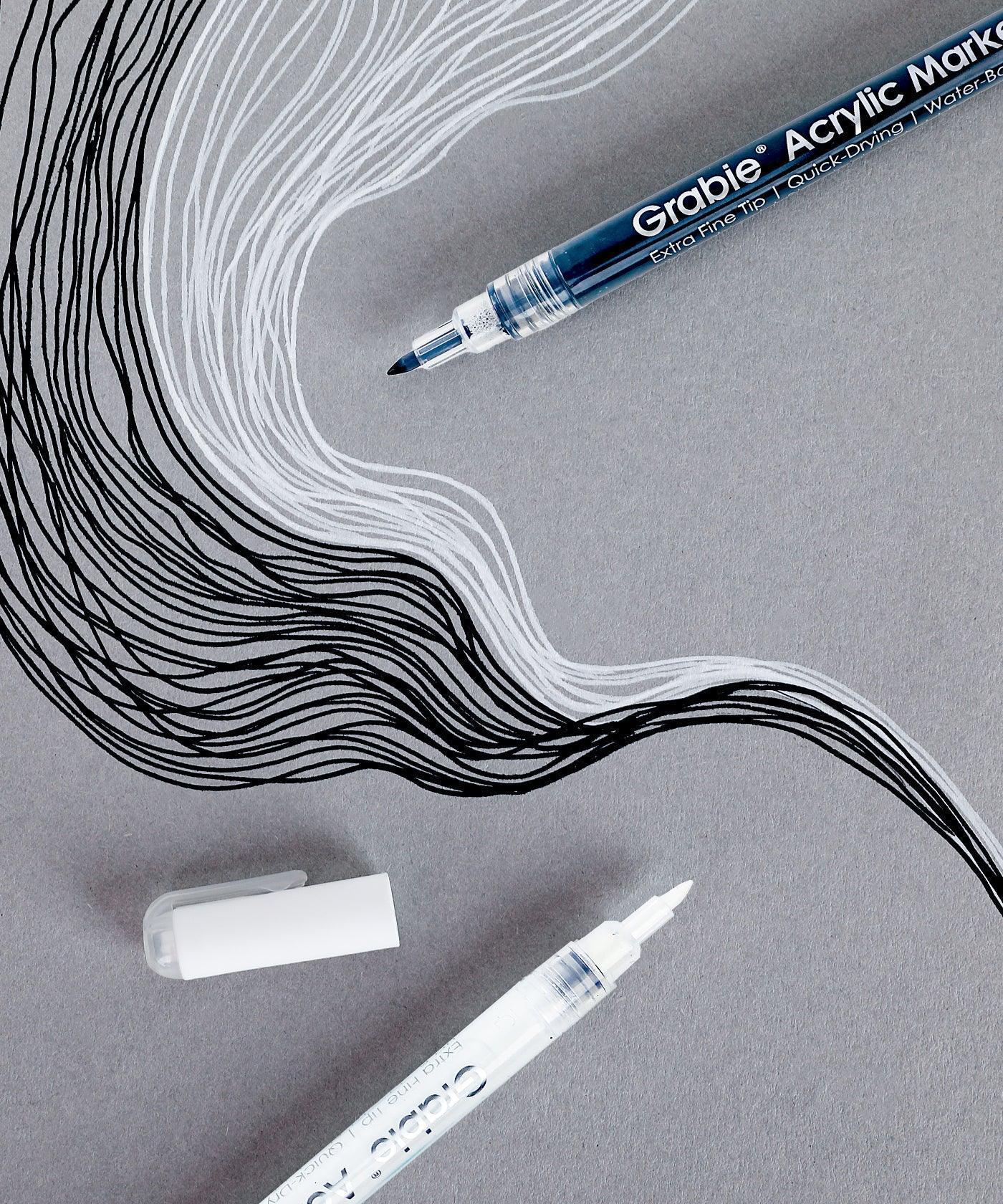 Extra Fine Tip Acrylic Paint Marker Set Of 6 with black and white ink creating detailed flowing lines on gray paper.