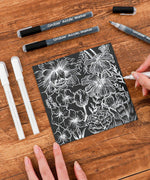 Grabie Acrylic Paint Marker Set used to create detailed white floral design on black paper for scrapbooking or art supplies