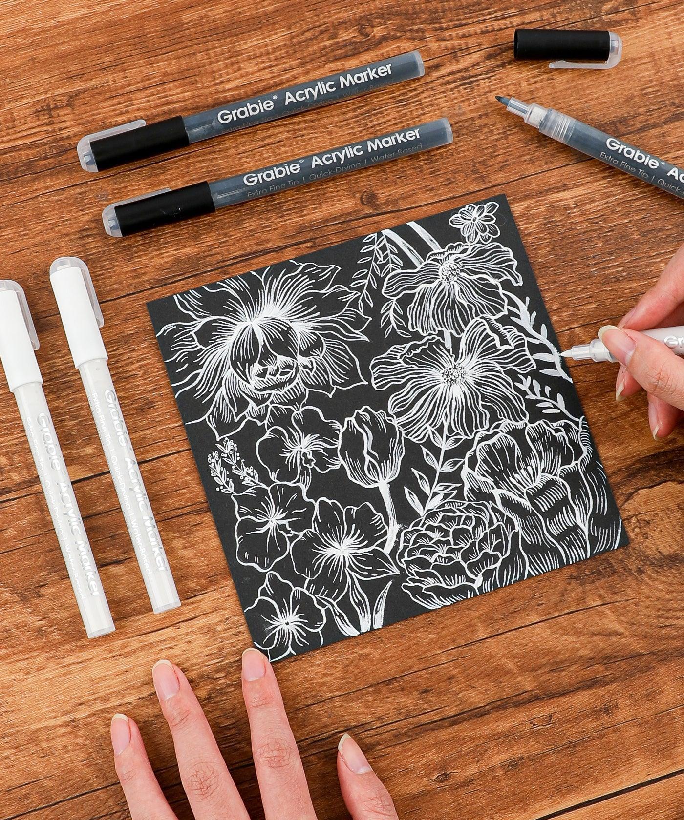 Grabie Acrylic Paint Marker Set used to create detailed white floral design on black paper for scrapbooking or art supplies