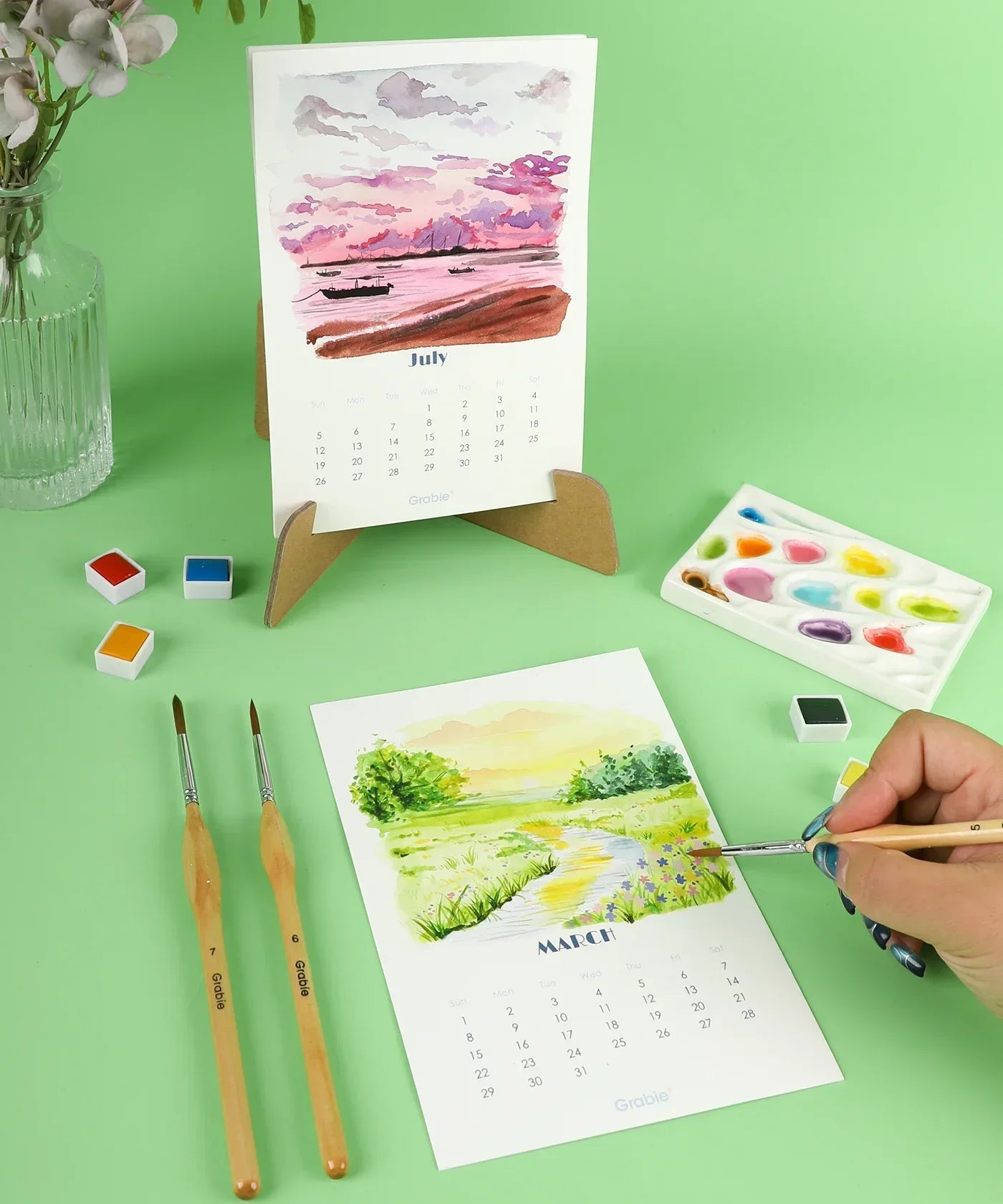 12-Month Watercolor Calendar Set For 2026 with hand-painted landscapes and watercolor art supplies on green background