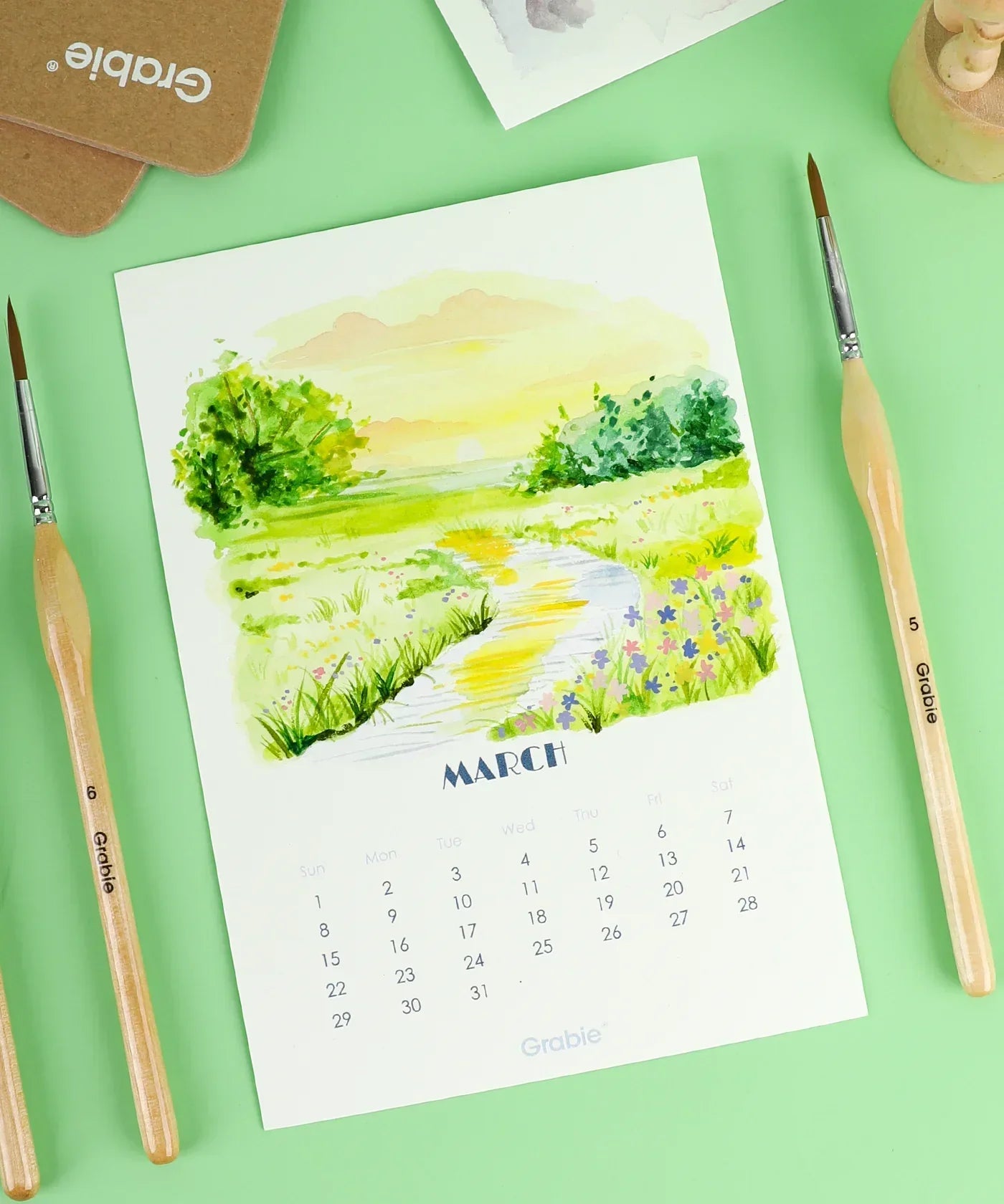 March page of the 2026 Watercolor Calendar & Creative Tools Set featuring a scenic watercolor landscape with art brushes.