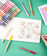 Colorful hand-drawn doodles being created with Grabie Acrylic Paint Marker Set on white paper against a green background