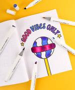 Open coloring book with a colorful "Good Vibes Only" design and Dual Tone Brush Tip Acrylic Paint Marker Set With Coloring Book markers nearby