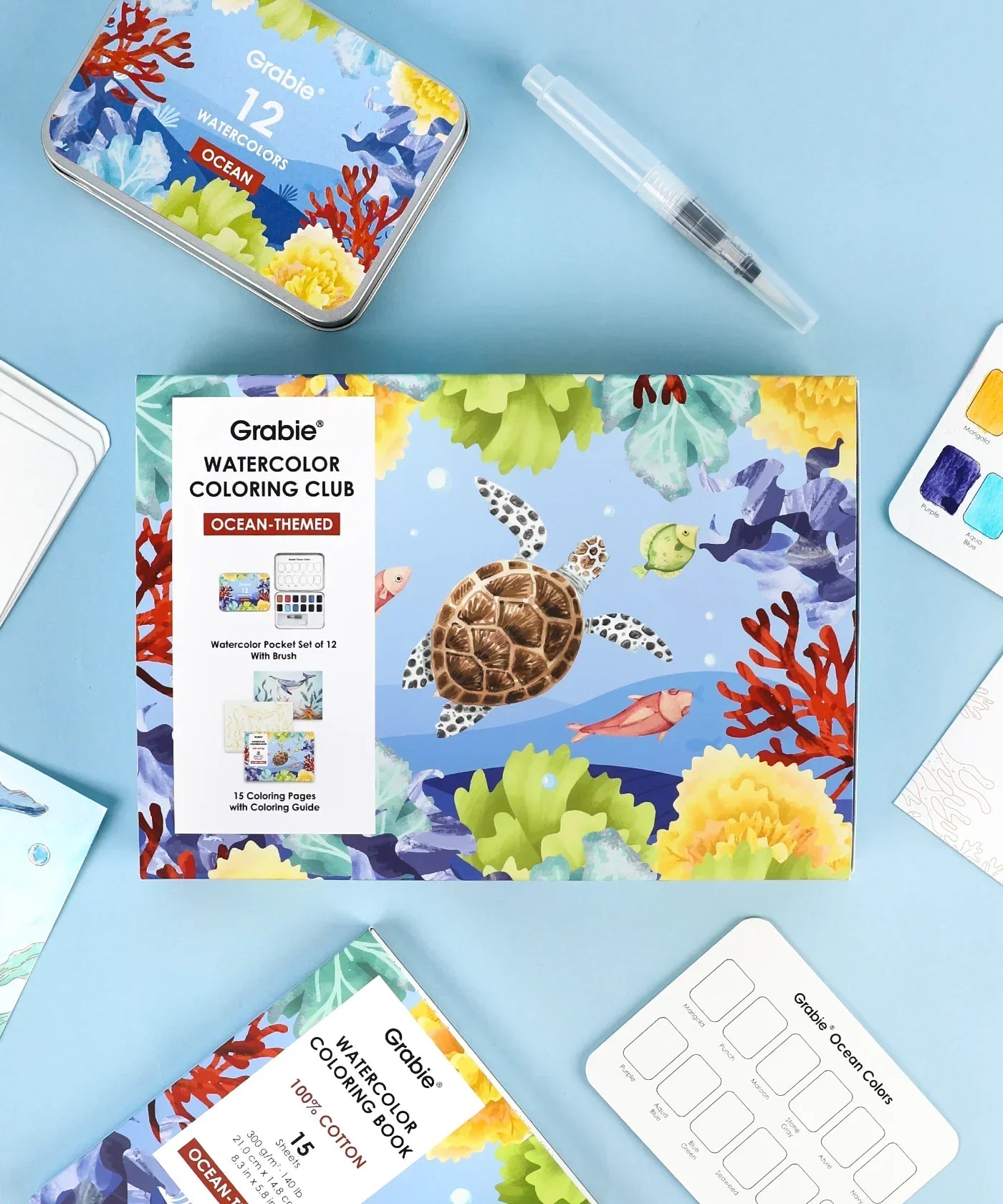 Ocean-Themed Watercolor Coloring Club Box with ocean illustrations, watercolor set, brush pen, and coloring pages laid out on blue background