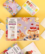 Grabie Quarterly Watercolor Coloring Club with dessert-themed watercolor set, brushes, and coloring pages on yellow background