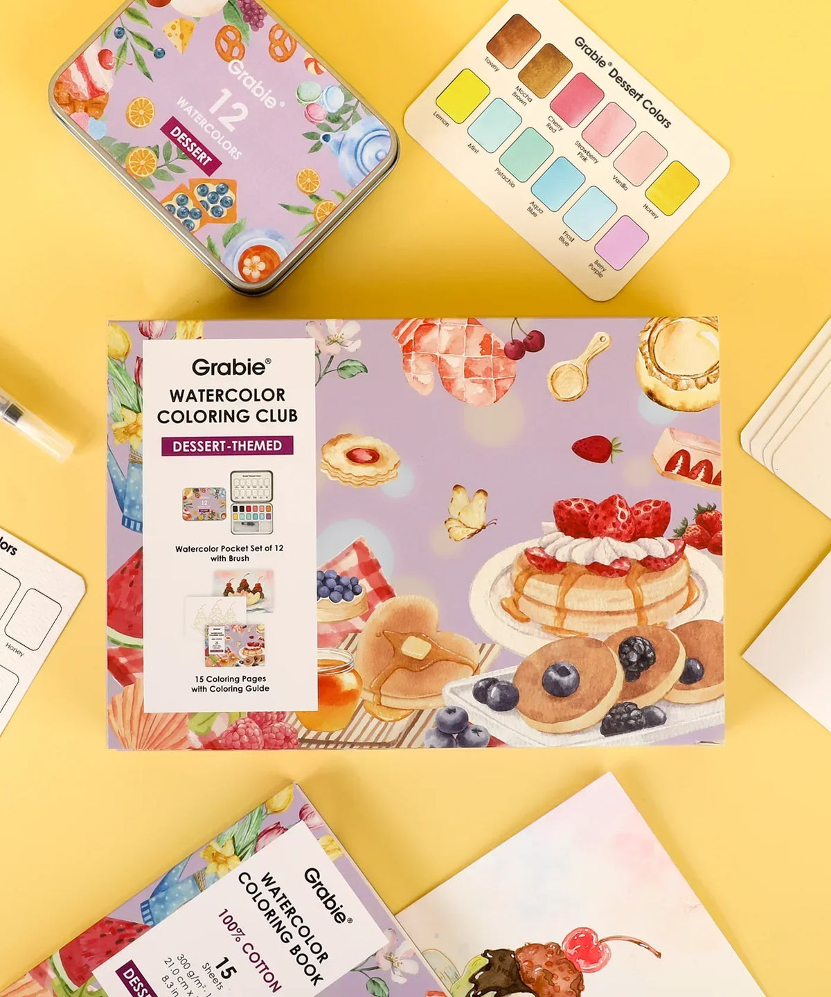 Grabie Quarterly Watercolor Coloring Club with dessert-themed watercolor set, brushes, and coloring pages on yellow background