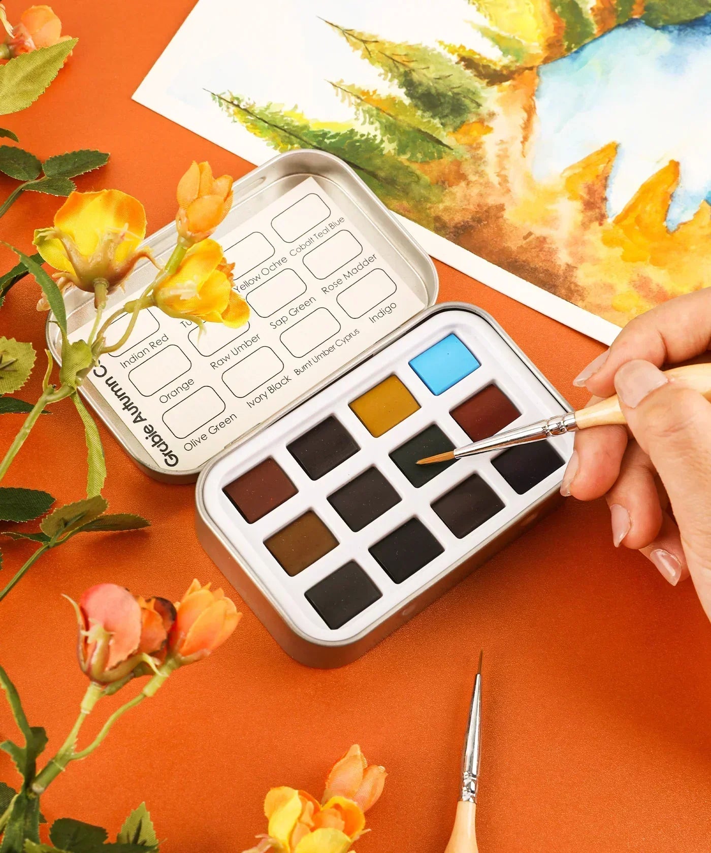 Watercolor Pocket Set - 5 Themes Value Bundle with assorted autumn colors and a paintbrush in use on orange surface