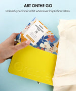 Hand placing floral watercolor pad into yellow case with canvas bag for 2026 Watercolor Calendar & Creative Tools Set