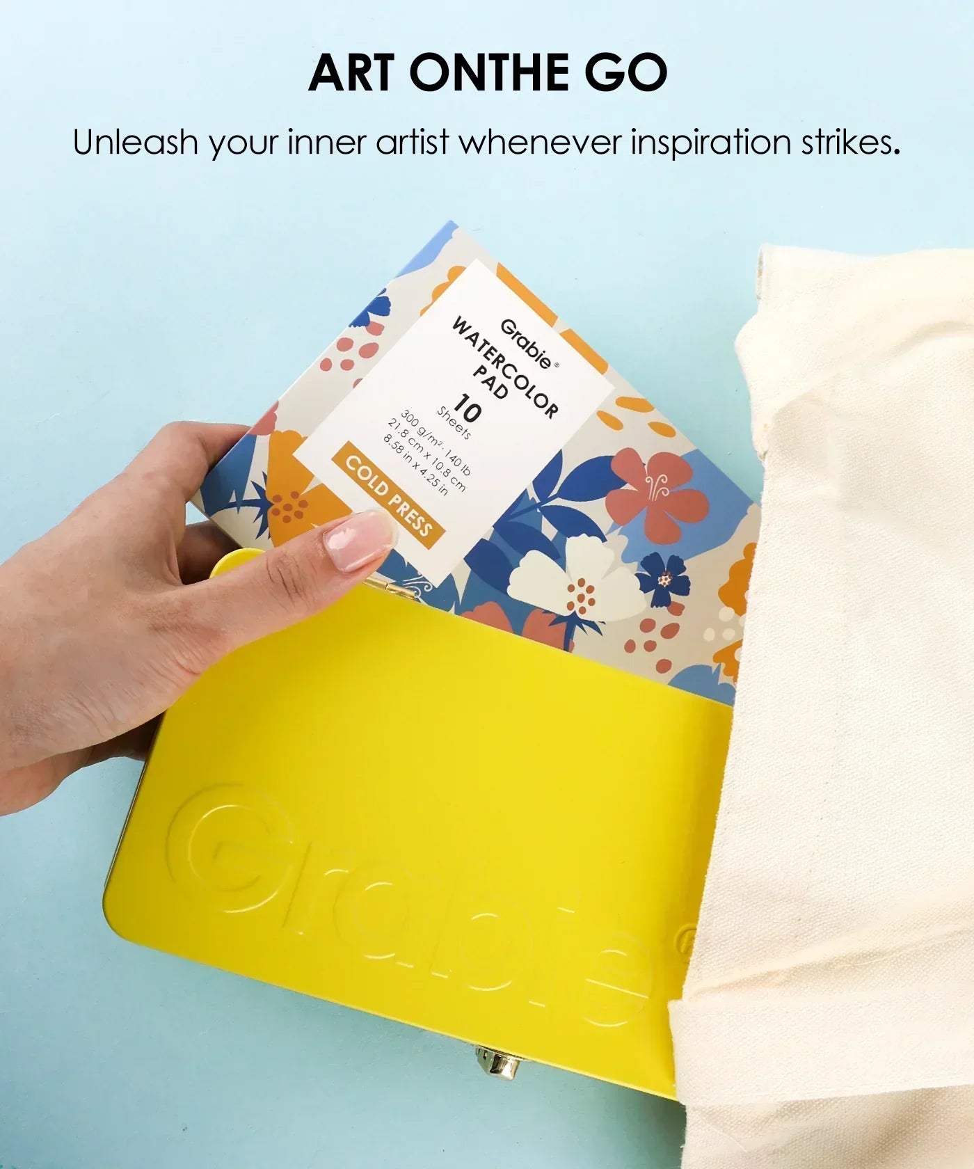 Hand placing floral watercolor pad into yellow case with canvas bag for 2026 Watercolor Calendar & Creative Tools Set