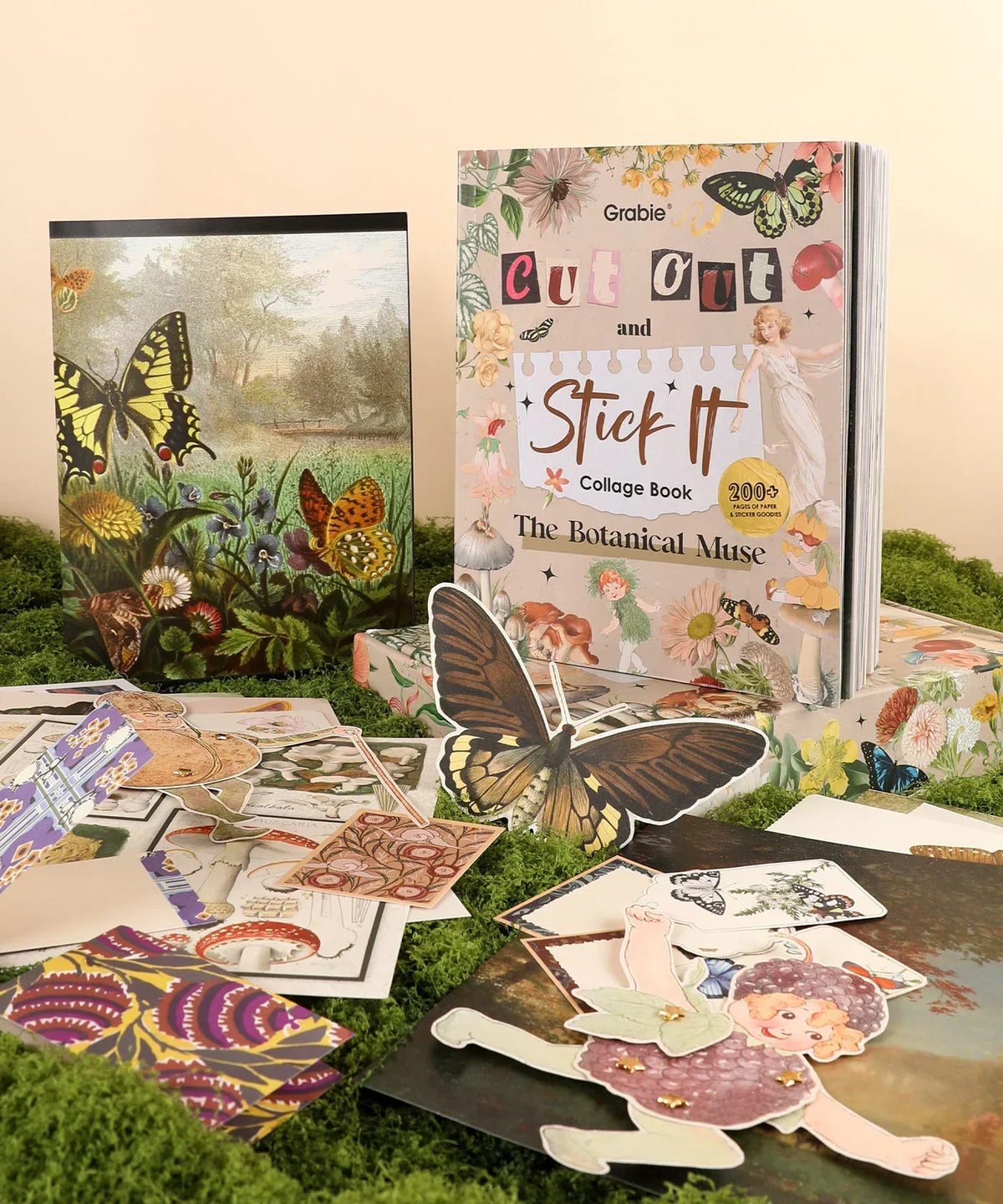 The Botanical Muse-Themed Grabie Scrapbook Club Box with butterfly, flower cutouts, and collage art supplies on moss background.
