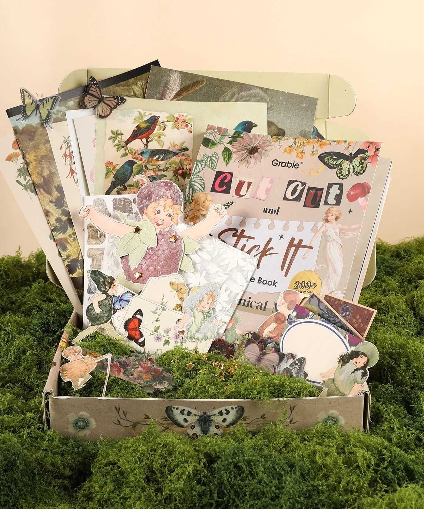 The Botanical Muse-Themed Grabie Scrapbook Club Box with vintage floral and bird cutouts, art supplies, and stickers on moss background