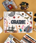 Threads Of Time-Themed Grabie Scrapbook Club Box with sewing and crafting supplies on a tan background