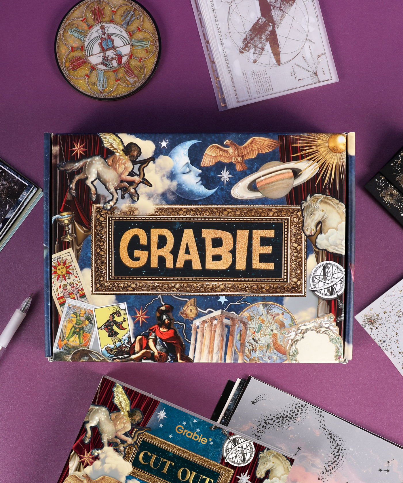 Grabie Scrapbook Club Box with celestial and mythological art supplies and scrapbook materials on a purple background