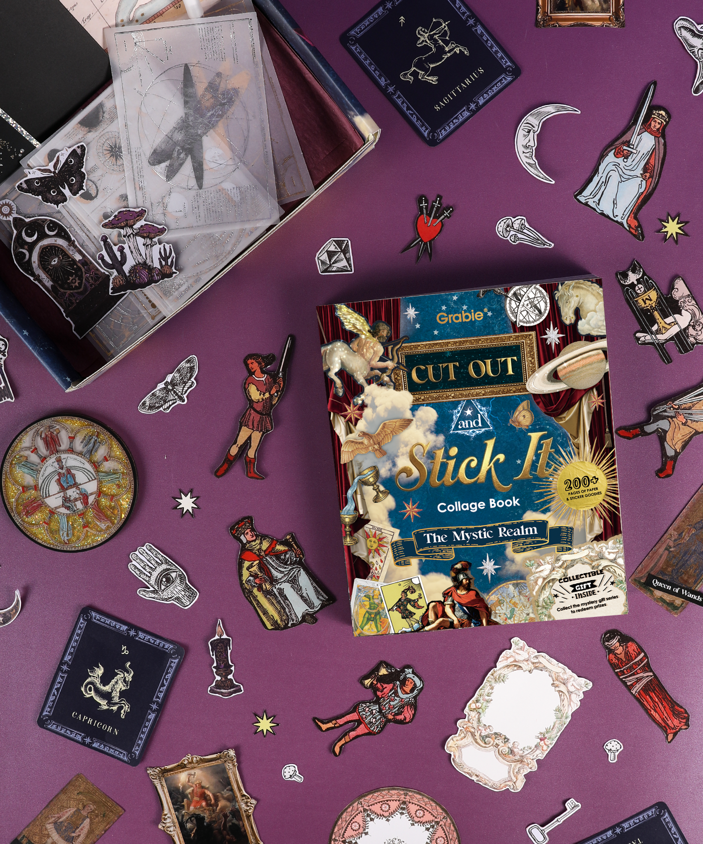 Grabie Scrapbook Club Box with mystical collage book and assorted vintage-style stickers and art supplies on purple background