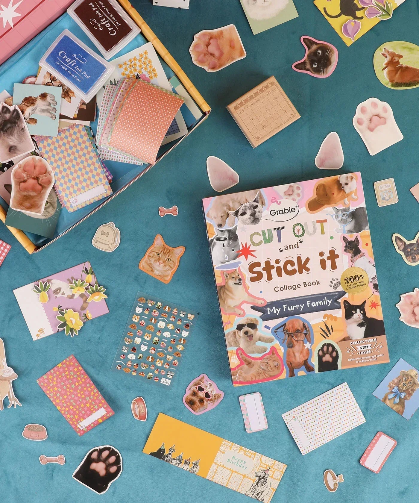 My Furry Family-Themed Grabie Scrapbook Club Box with pet stickers, patterned papers, and crafting supplies spread out on blue surface