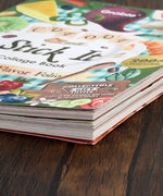 Close-up of a colorful, thick book titled 200+ Pages The Flavor Folio Collage Activity Book on a wooden surface
