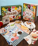 The Flavor Folio-Themed Grabie Scrapbook Club Box with colorful collage materials and art supplies on a wooden table