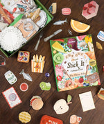 The Flavor Folio-Themed Grabie Scrapbook Club Box with assorted food-themed scrapbook stickers and cutouts on a wooden surface