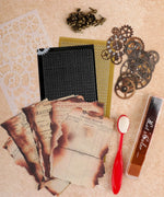 Grabie Scrapbook Club Box with vintage papers, metal gears, stencil, brads, red applicator, and ink blending tool for crafts