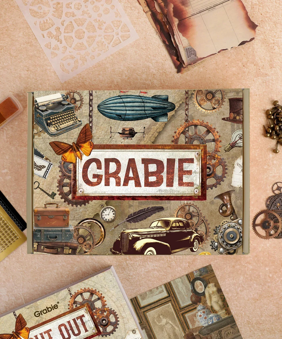 Vintage steampunk-themed Grabie Scrapbook Club Box surrounded by gears, butterflies, typewriter, and vintage items.
