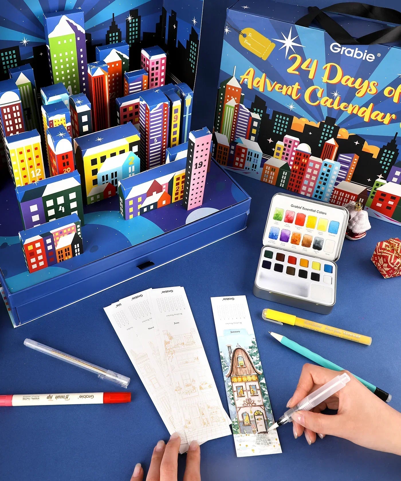 2025 Limited Edition Holiday Advent Calendar with colorful building blocks, art supplies, and a watercolor set on blue surface
