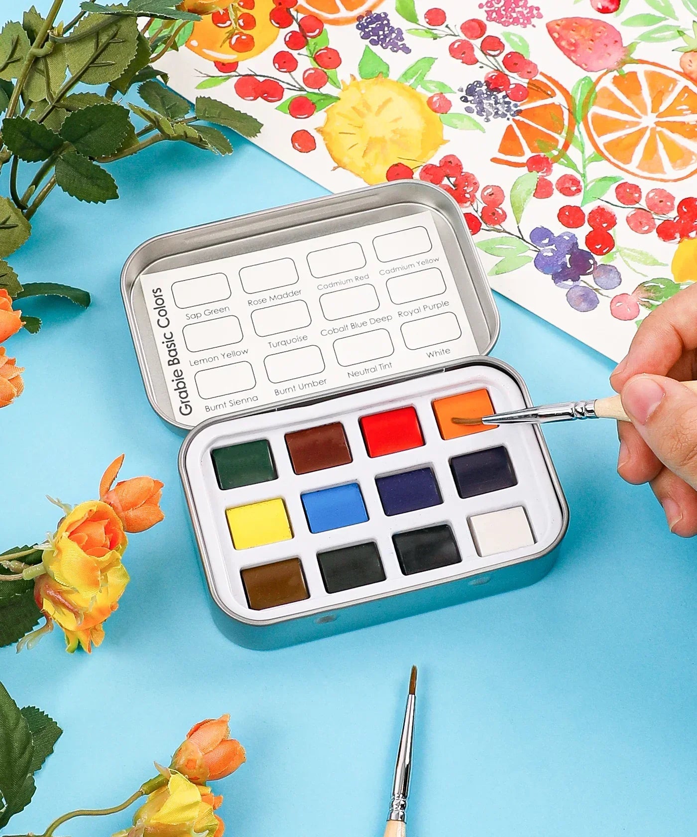 Watercolor Pocket Set of 12 - Essential Colors in a tin with a hand painting vibrant floral watercolor artwork nearby