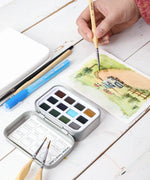 Watercolor Pocket Set of 12 - Forest Colors being used for painting a landscape with brushes and art supplies nearby