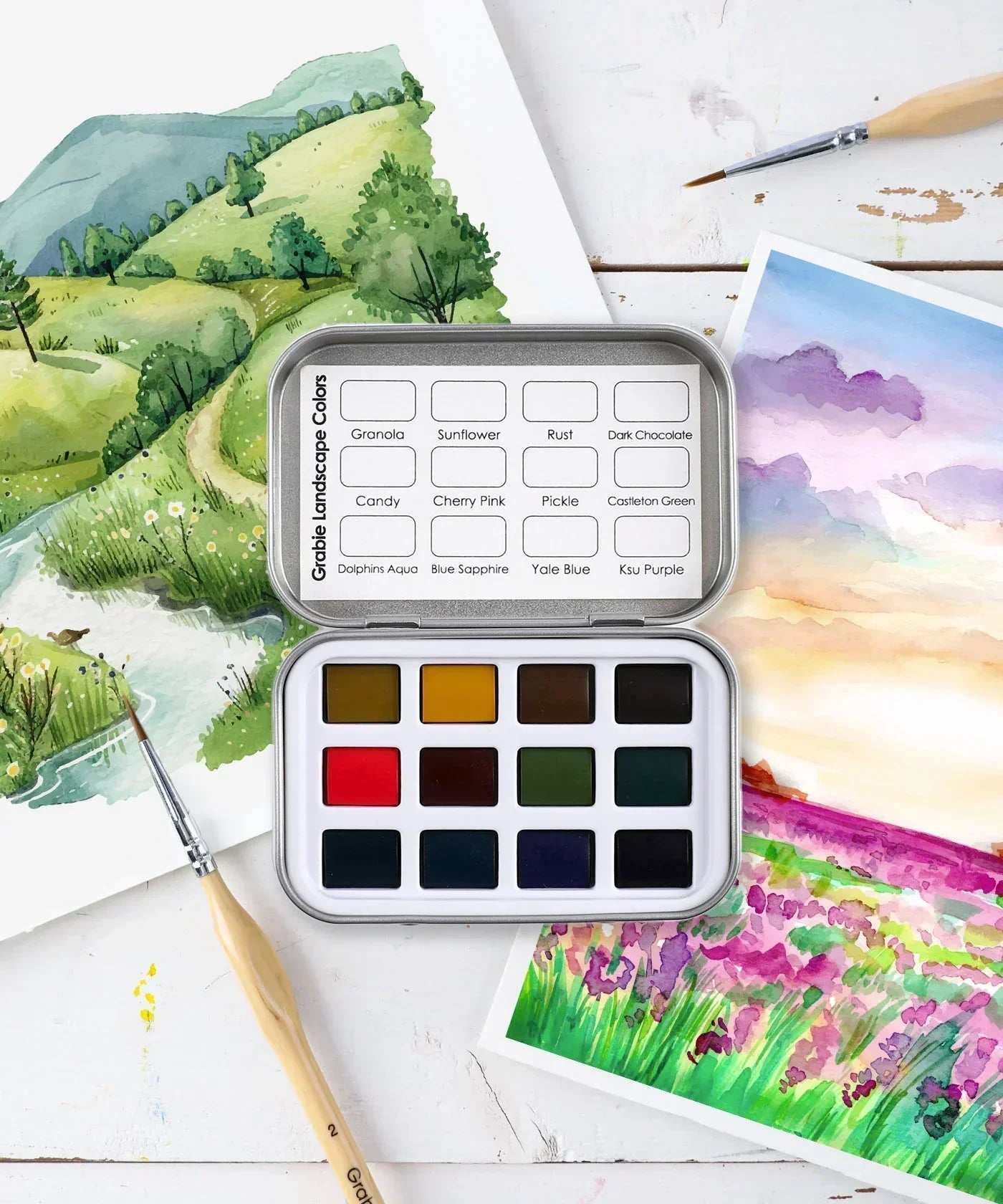 Watercolor Pocket Set of 12 - Landscape Colors with vibrant green, purple, and brown shades beside watercolor landscape paintings and brushes