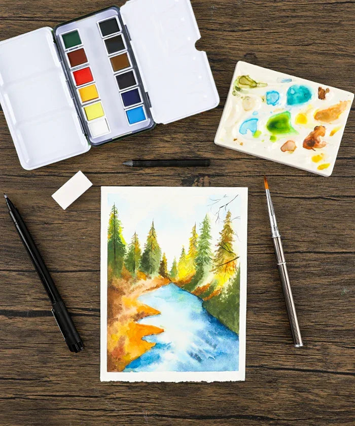 Grabie x @SSavaArt Watercolor 12 Half Pan Deluxe Travel Set with brush, palette, and forest river landscape painting on wood table