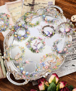 24 Pcs Grabie Exclusive Bunnies and Blooms Sticker Set with floral wreaths, pastel eggs, and cute bunny illustrations on a vintage tray