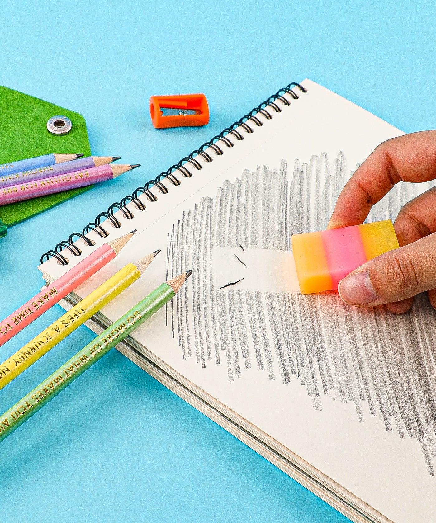 Hand erasing pencil marks on sketchbook page with Colorful Inspirational Sketch Pencil Set and sharpener nearby