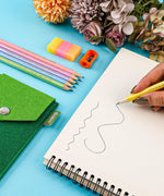 Colorful Inspirational Sketch Pencil Set with pastel pencils, sharpener, eraser, and hand sketching on paper next to flowers