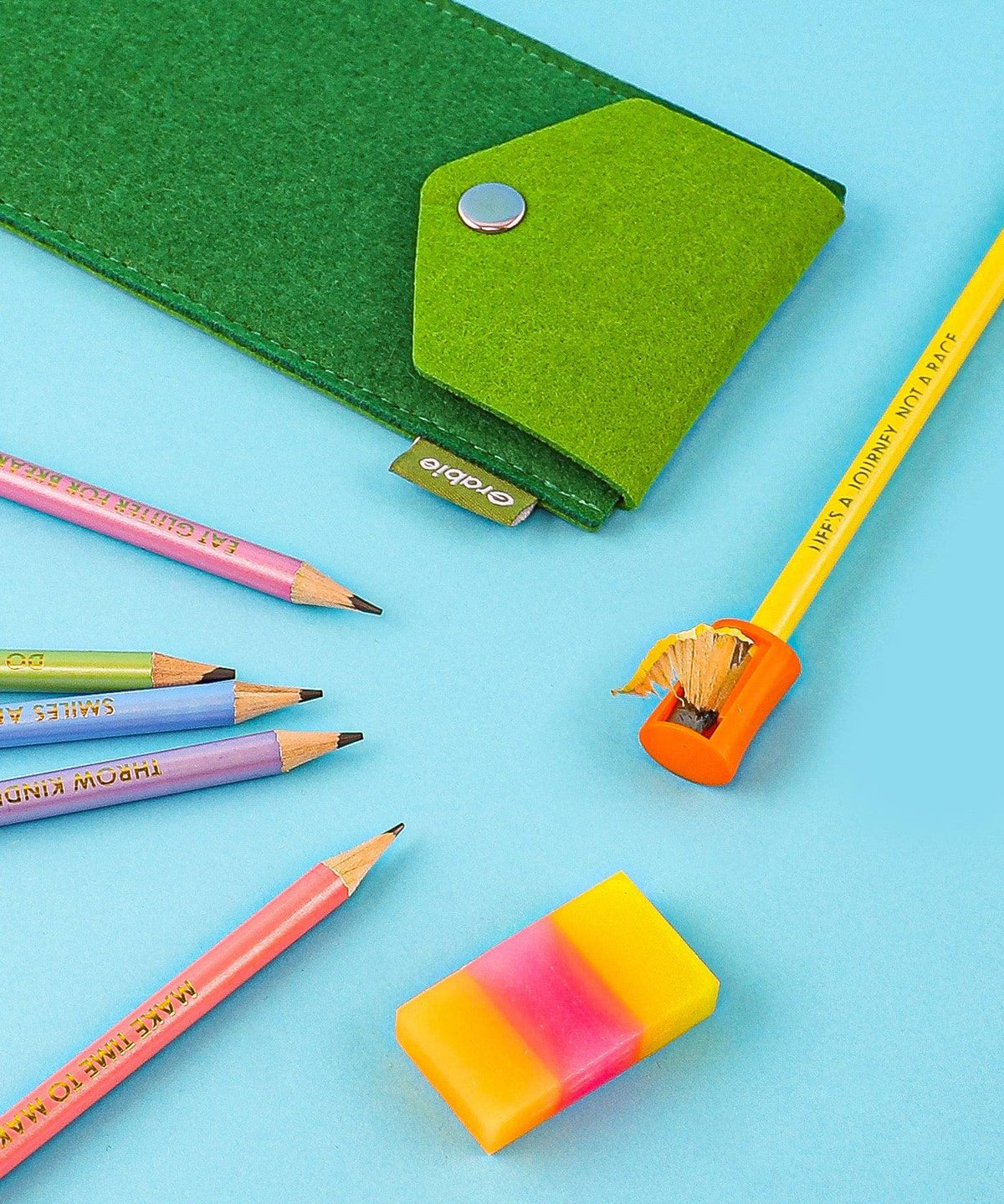 Colorful Inspirational Sketch Pencil Set with sharpened pencils, sharpener, eraser, and green felt pencil case on blue background