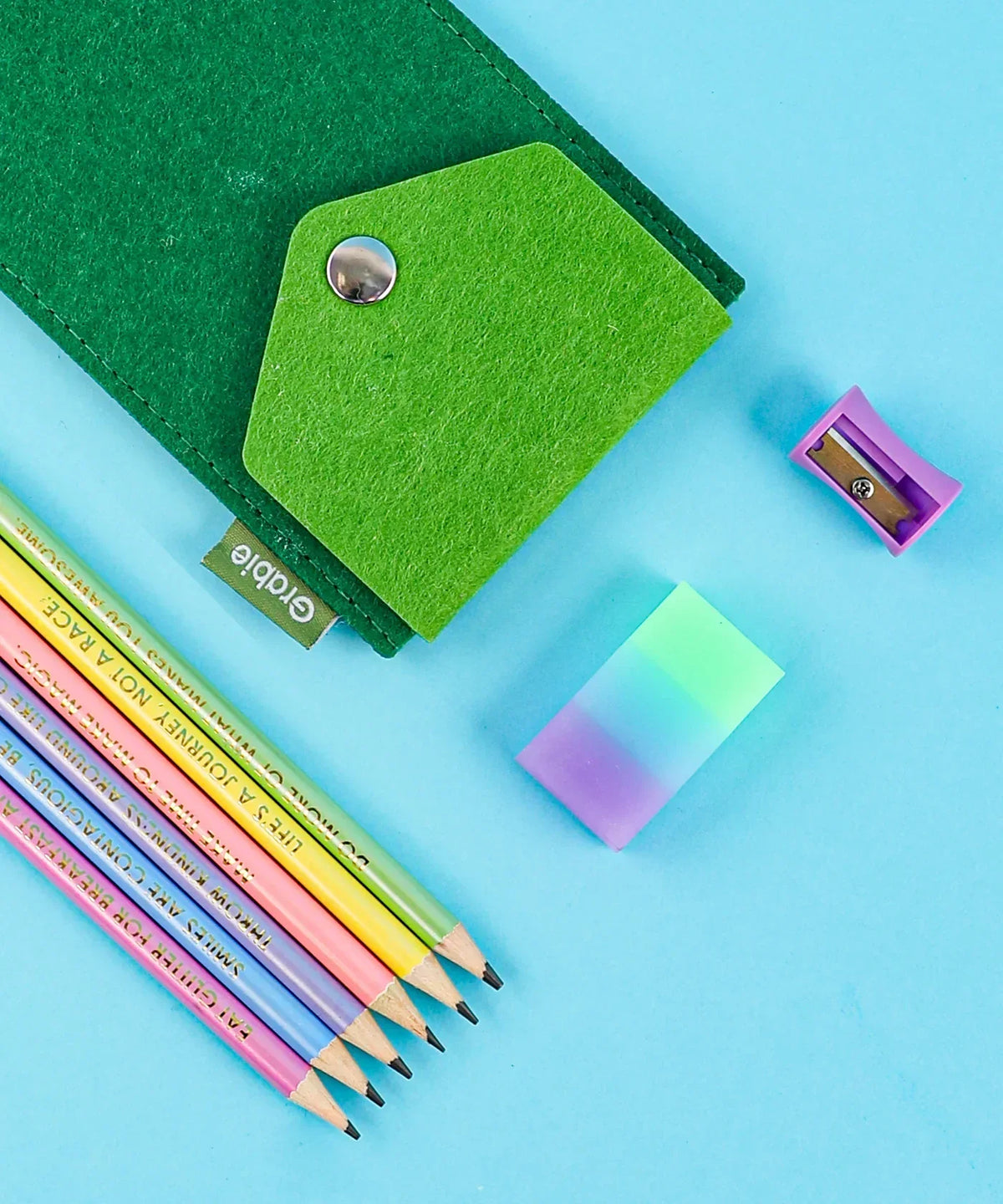 Let Your Feelings Flow Grabie Art Club Box with colorful pencils, eraser, sharpener, and green felt pouch on blue background