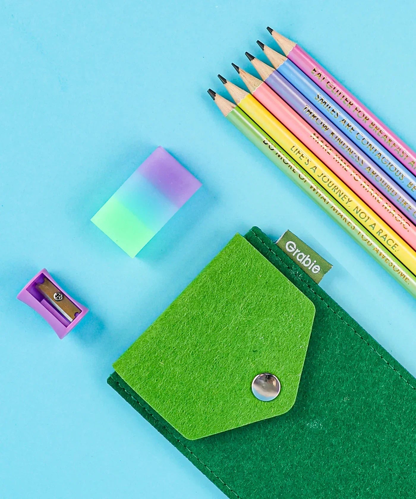 Colorful Inspirational Sketch Pencil Set with pastel pencils, a gradient eraser, sharpener, and green felt pencil case on blue background