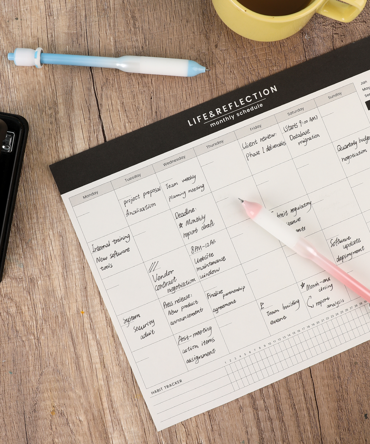 Pink and blue novelty fidget pens resting on a wooden desk next to a written monthly schedule planner.