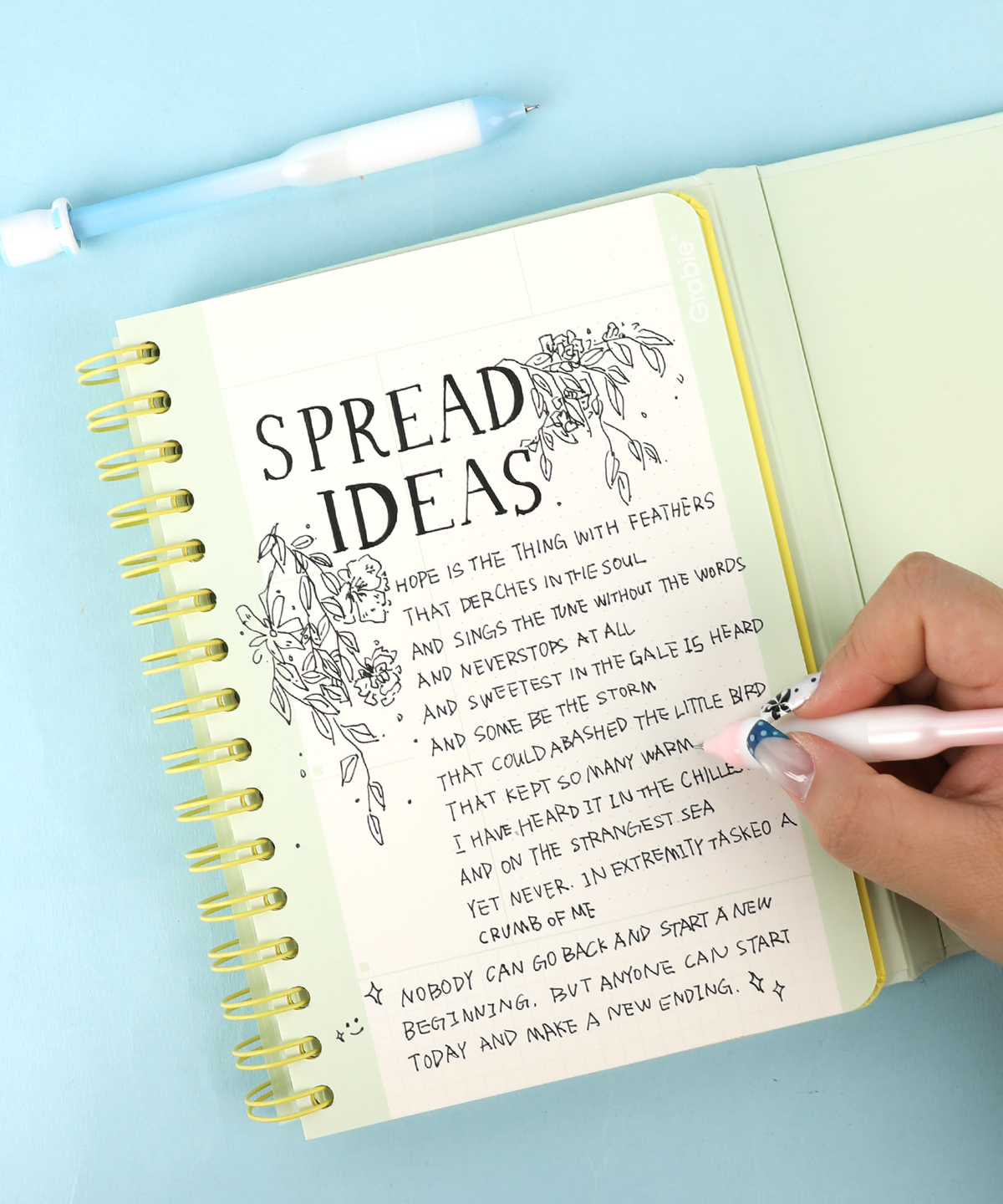Hand writing handwriting notes and floral doodles in an open notebook using a pastel pink fidget pen.