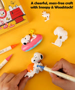 Hands painting a Snoopy and Woodstock resin figure with blue and orange dual tip markers.