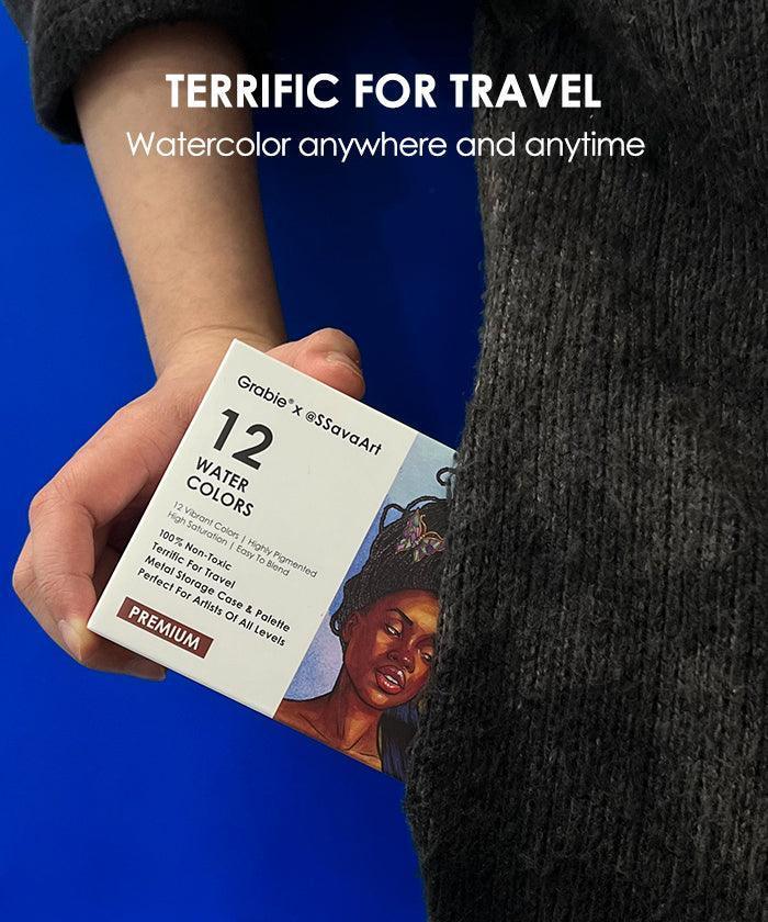Hand holding a 12 color watercolor travel set with illustrated box, ideal for artists on the go